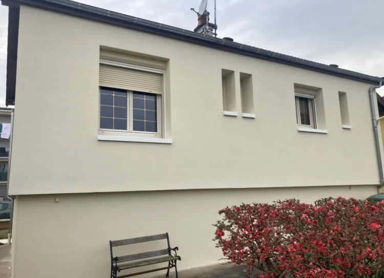 Façade enduite claire après isolation par l'extérieur, banc et arbuste fleuri