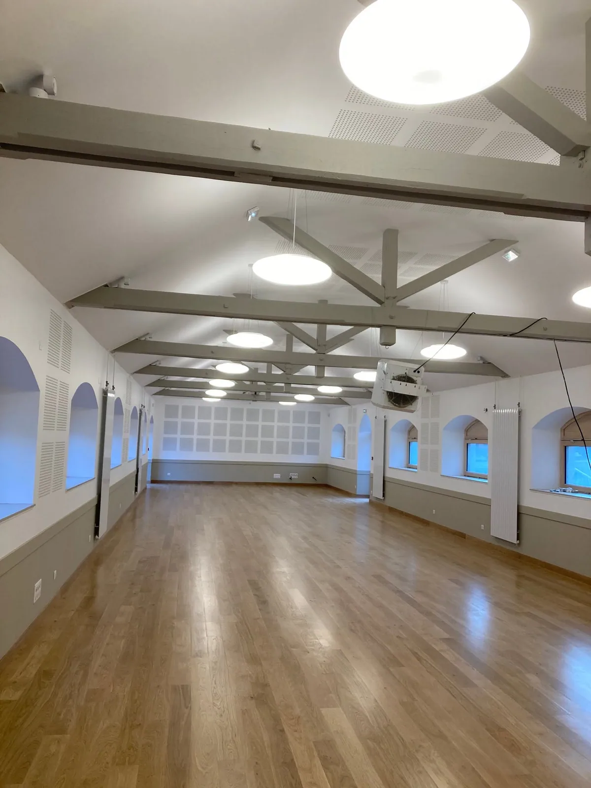 Salle des fêtes repeinte, murs clairs, charpente apparente et parquet