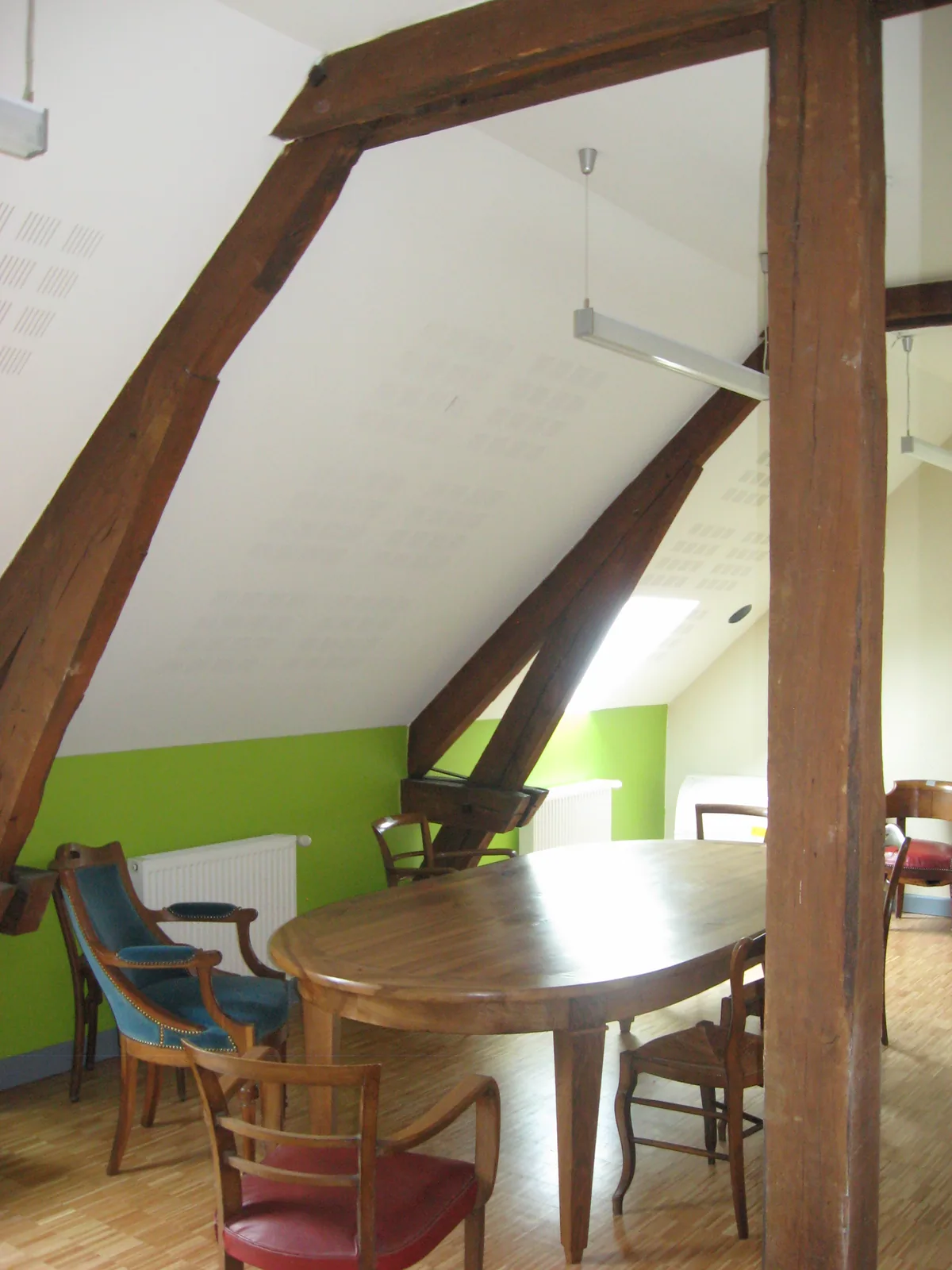Salle sous combles aux murs vert anis et poutres apparentes