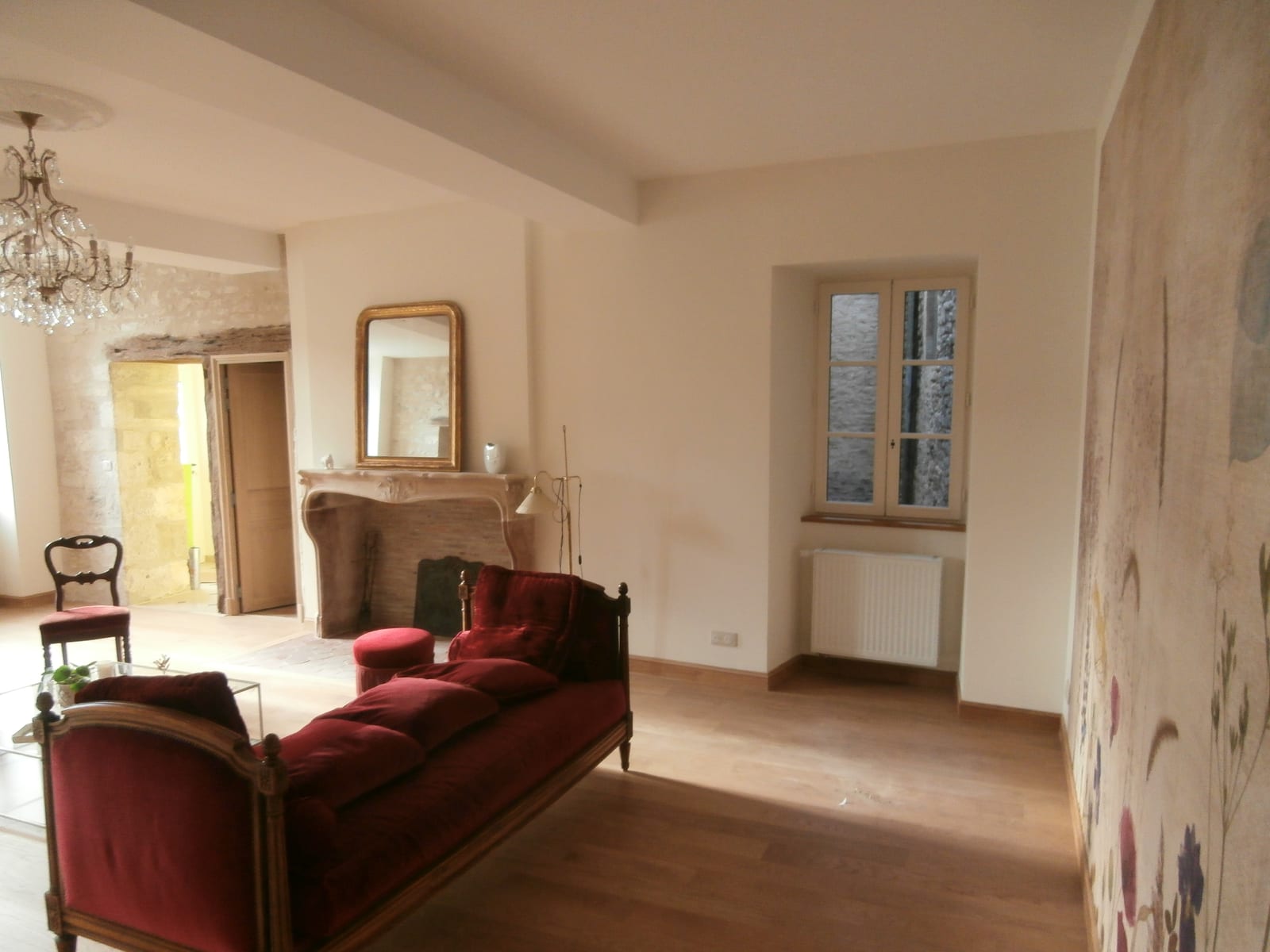 Salon aux murs peints en gris clair, moulure de plafond blanche, canapé rouge devant un panneau mural fleuri