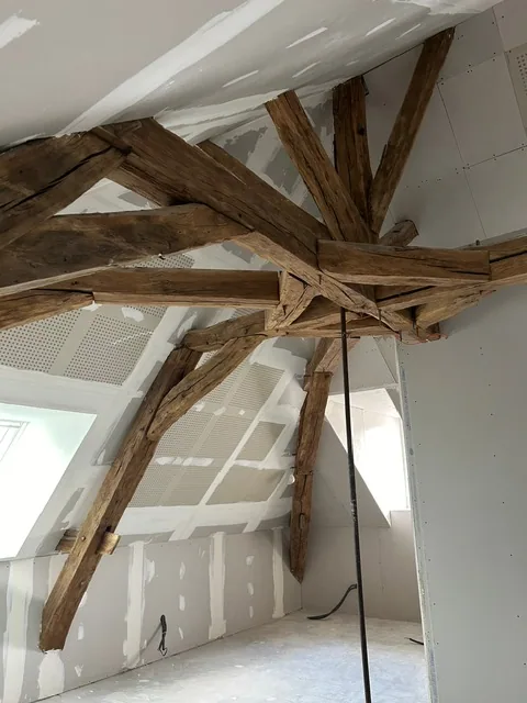 Combles aménagés sous une charpente ancienne conservée, plaques de plâtre en cours de finition